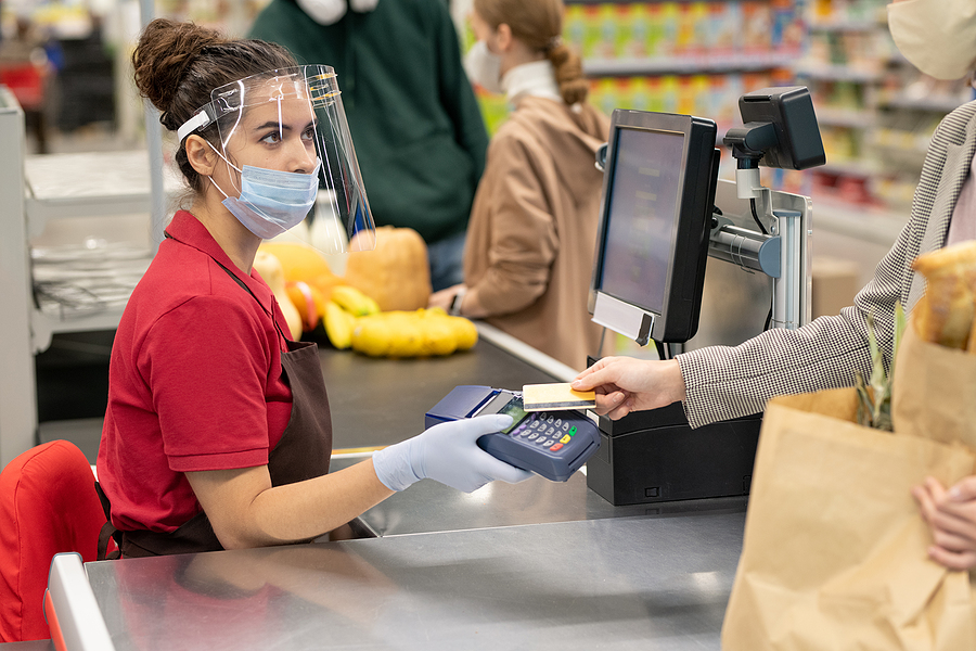 Cashier in COVID protective gear accepts payment